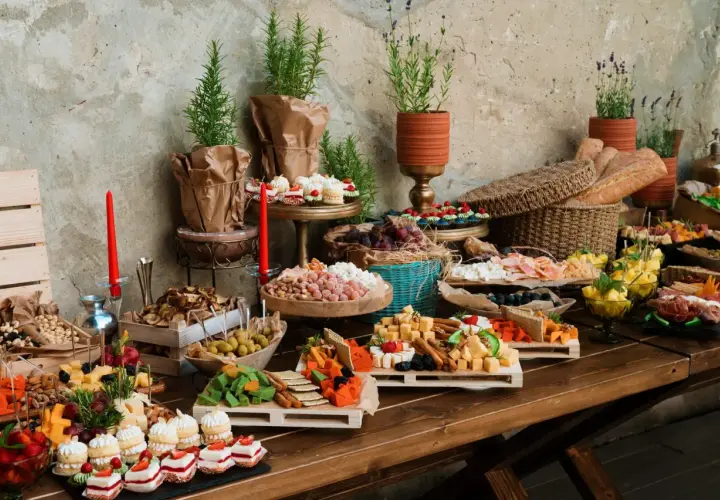 Stół z bogatym cateringiem: sery, wędliny, owoce, ciastka, pieczywo i dekoracje.