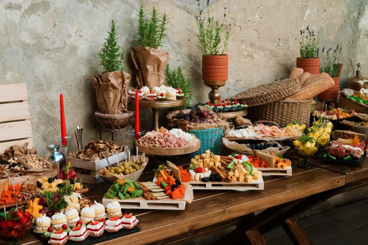 Stół z bogatym cateringiem: sery, wędliny, owoce, ciastka, pieczywo i dekoracje.